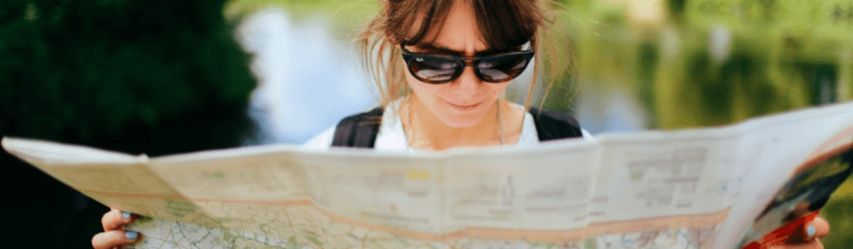 A woman wearing sunglasses is looking at a paper map