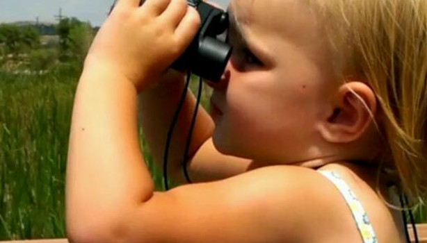 A little girl gazes intently through binoculars at the world.