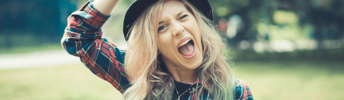 A blonde woman shouts with glee while tipping her hat.