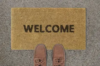 A plain doormat with the words "Welcome". a pair of men's loafers are partially on the mat.