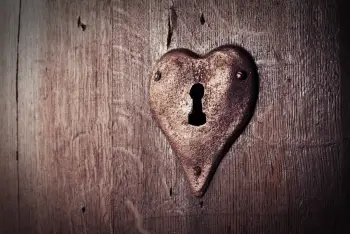 A rusty hart shaped lock with a keyhole in the center is mounted on a weathereed door.