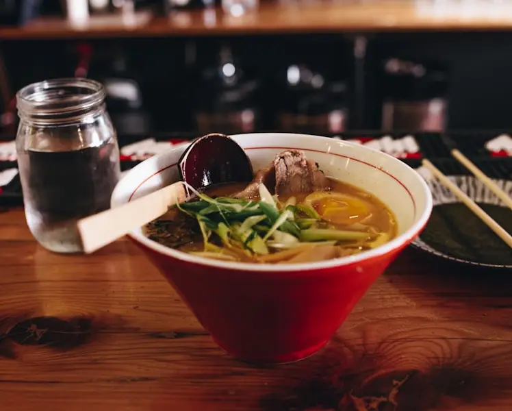 A bowl of healthy pho soup with a small plate and chopstix closeby.