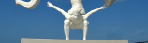 White statue of a man bent down, arms outstretched with a white elephant on his back with the elephant balancing on his front legs.