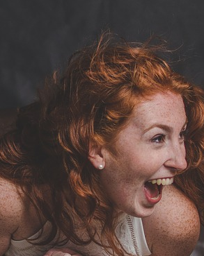 A red haired woman bends over in laughter as she looks ahead at what made her laugh
