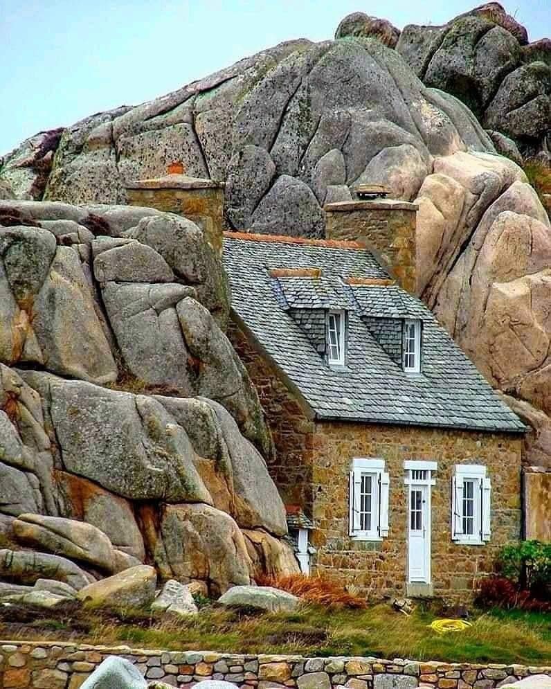 A small house is built within a massive stone mountain. Only the top of the roof and the front of the house are visible.